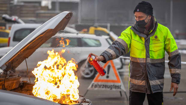 Ein Mann löscht mit dem Handfeuerlöscher einen Brand im Motorraum