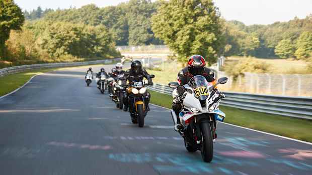 Eine Gruppe von Motorradfahrern fährt auf einer Straße, umgeben von Bäumen und grüner Landschaft.