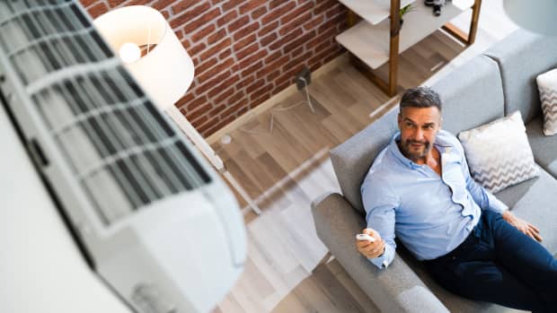 Ein Mann auf einer Couch, bedient Klimaanlage in seinem Wohnzimmer