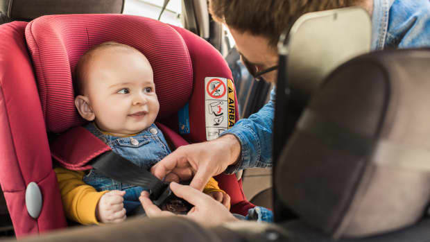 Vater schnallt sein kleines Baby auf dem Kindersitz an