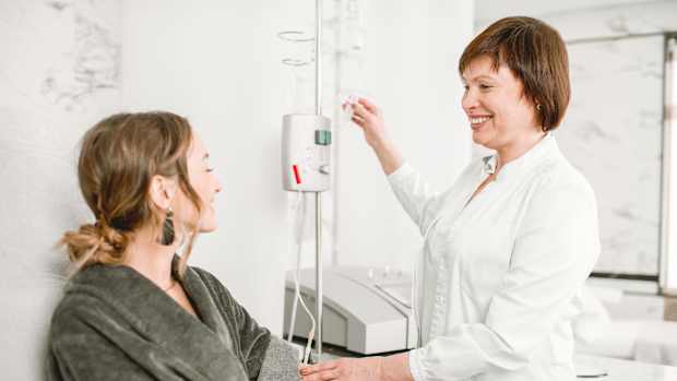 eine junge Frau in einem grauen Bademantel bekommt eine dialyse von einer Krankenschwester