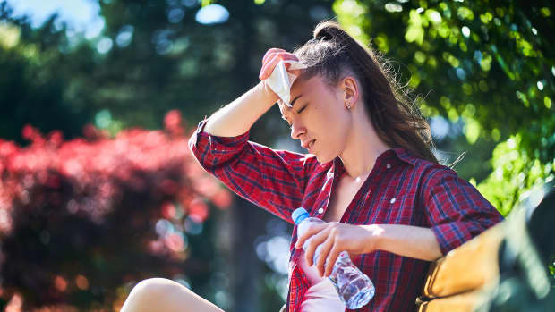 Junge Frau sitzt mit einer Wasserflasche in der Hand auf einer Parkbank