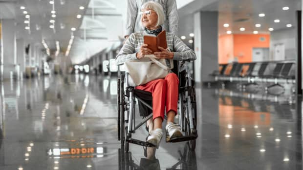 Mann im Rollstuhl holt seinen Koffer vom Gepäckband im Flughafen