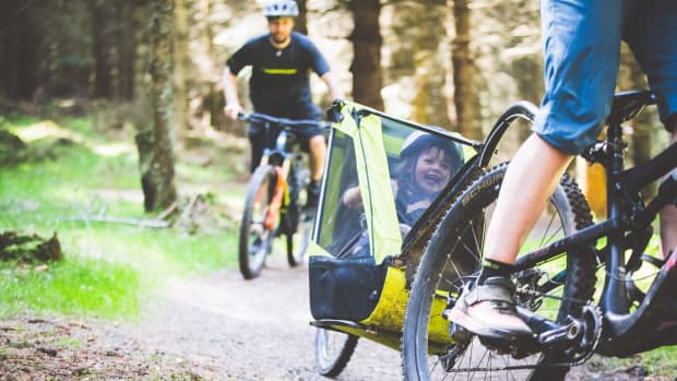fröhlich lachendes Kind im Fahrradanhänger eines Mountainbikes bei einer fahrt durch den Wald