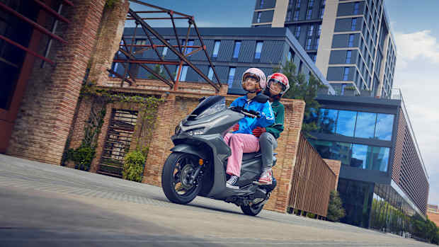 Zwei junge Frauen auf einem Honda Motorroller in einem urbanen Umfeld