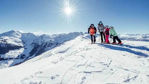 Eine Familie mit Skiern im Schnee im Hintergrund sieht man die Kitzbühler Alpen