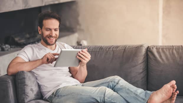 Ein Mann liegt auf dem Sofa mit einem Tablet in der Hand