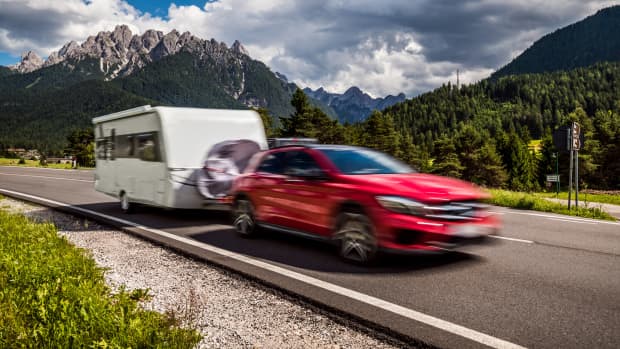 Ein rotes Auto zieht einen Wohnwagen vor einer Bergkulisse