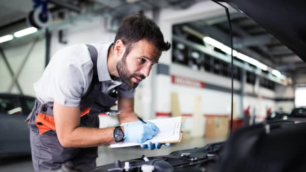 Mechaniker steht am Motor eines Autos in einer Werdkstatt und schreibt etwas auf