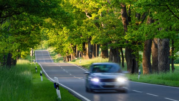 Auto mit eingeschalteten Scheinwerfern fährt auf Landstrasse