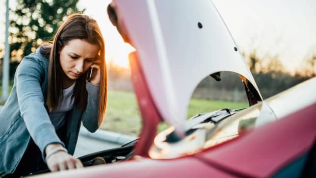 Junge Frau telefoniert beim Blick in die Motorhaube weil ihr Auto nicht anspringt