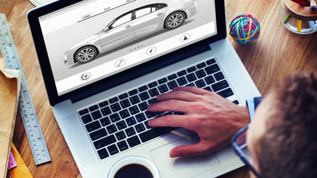 Ein Mann sitzt an einem Laptop mit einer Tasse Kaffee in der Hand und schaut auf ein Auto auf dem Bildschirm.