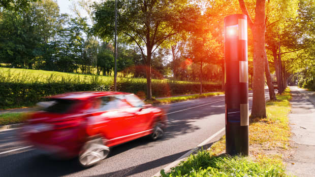 Rotes Auto an einer sommerlichen Landstrasse, das gerade geblitzt wird
