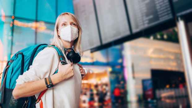 Eine blonde Frau mit Rucksack auf dem Rücken trägt eine Maske an einem Flughafen