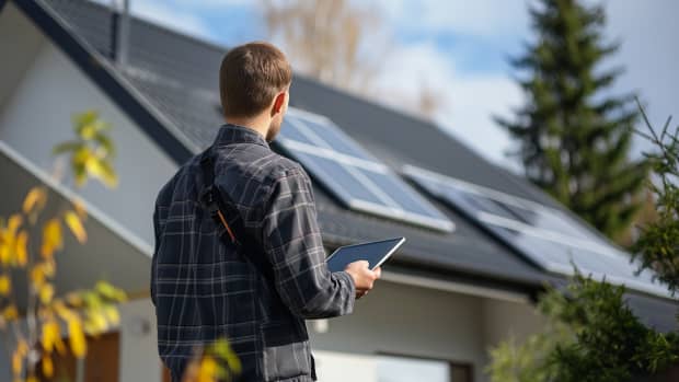 Ein Mann steht vor seinem Einfamilienhaus mit Solarpanele auf dem Dach