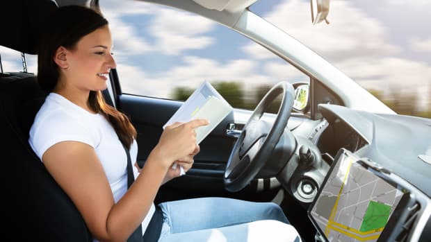 Frau liest ein Buch am Steuer eines Autos, das autonom fährt