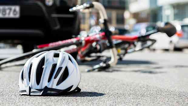 Ein Fahrradhelm und ein Fahrrad liegen nach einem Fahrradunfall vor einem Auto auf der Straße