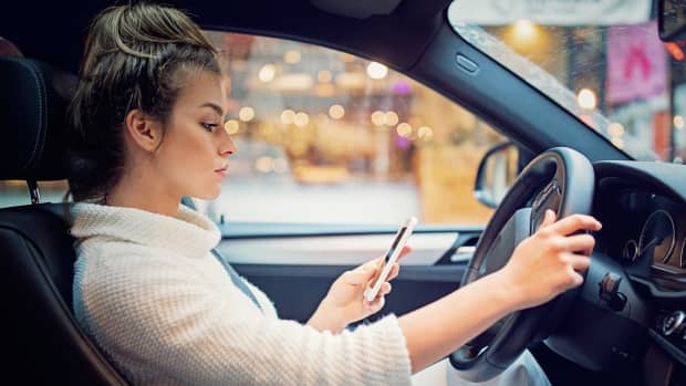 Frau schreibt während des Autofahrend auf ihrem Smartphone