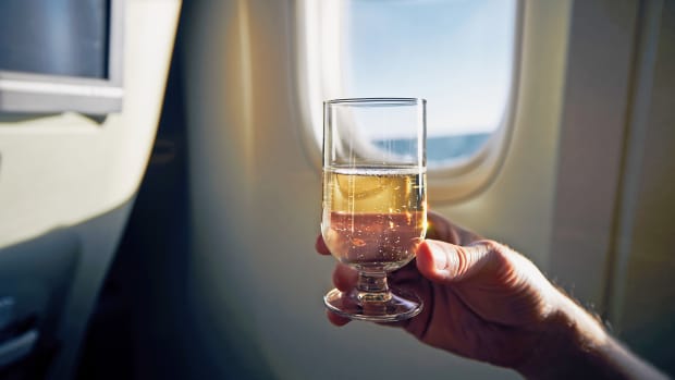 Eine Person hält ein Glas Wein im Flugzeug in der Hand