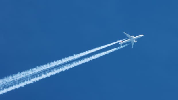 Flugzeug vor blauem Himmel mit langem Kondensstreifen
