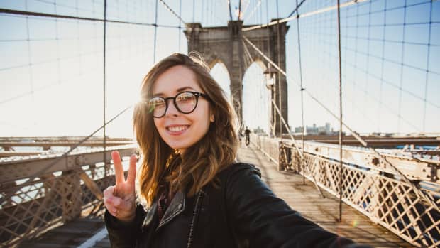 Eine junge Frau steht lachend auf der Brooklyn Bridge