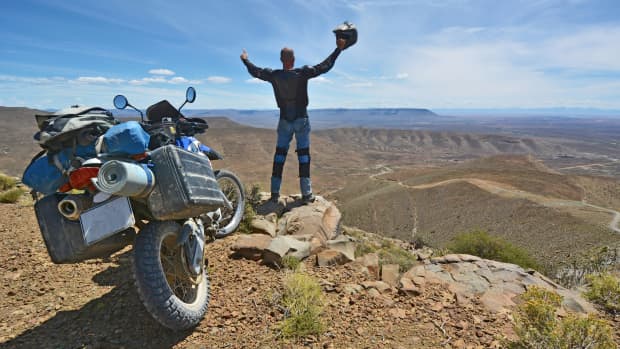 Ein Mann schaut über ein Tal und freut sich im Hintergrund parkt sein Motorrad