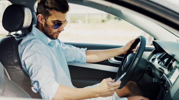 Mann schaut während der Autofahrt auf sein Handy