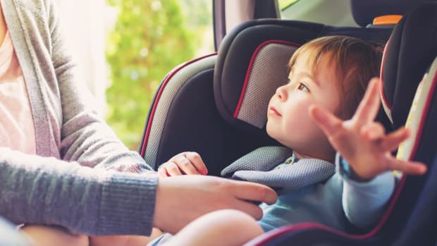 Kleinkind wird von Frau im Kindersitz angeschnallt