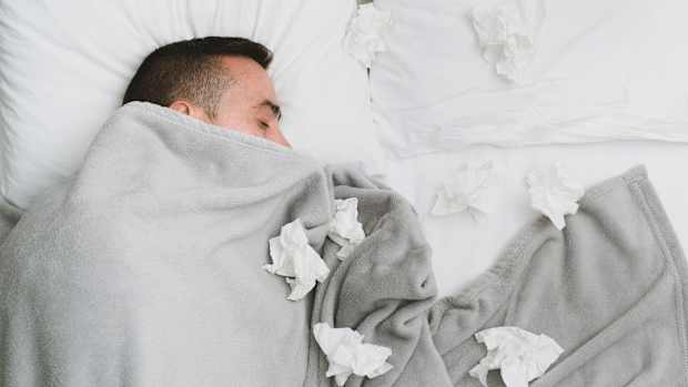 Ein Mann liegt mit vielen benutzen Taschentüchern krank im Bett