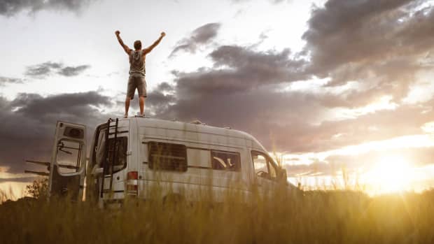 Mann mit erhobenen Armen auf seinem Wohnmobil