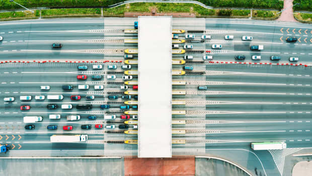 Eine Draufsicht auf eine stark befahrene Mautstraße mit vielen Autos, die anstehen, um die Autobahnmaut zu bezahlen