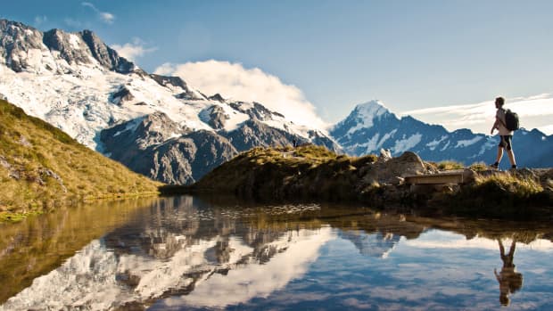Ein Wanderer läuft an einem See vorbei, im Hintergrund sieht man schneebedeckte Berge.