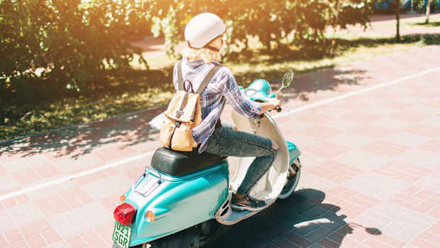 Eine Frau auf einer Vespa fährt auf einer Landstraße