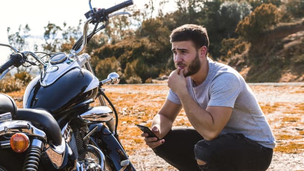 Mann kniet mit seinem Handy neben seinem Motorrad mit Panne