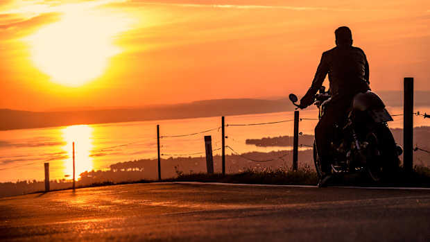 Ein Motorradfahrer fährt auf einer Straße bei Sonnenuntergang. Im Hintergrund ist der Bodensee zu sehen