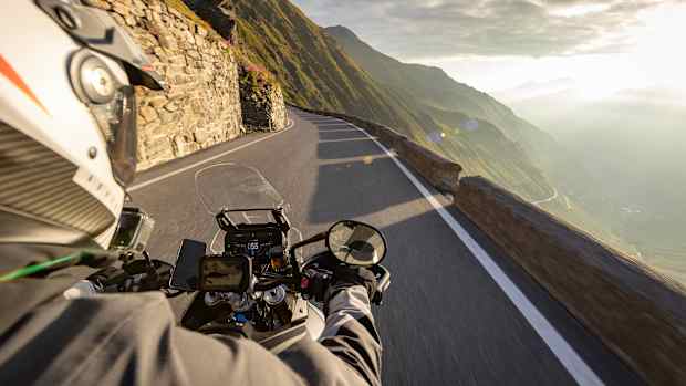 Motorradfahren in den italienischen Alpen bei Sonnenaufgang, Blick vom Lenker, dramatischer Himmel. Reisen und Freiheit, Aktivitäten im Freien