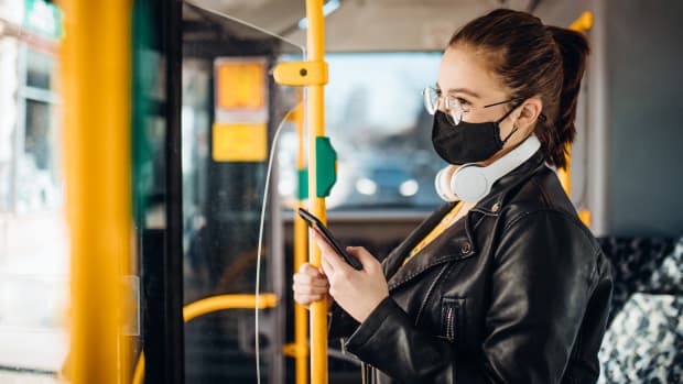 Junge Frau steht mit ihrem Handy in einem Bus