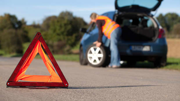 Eine Frau mit Warnweste wechselt den Reifen an ihrem Auto