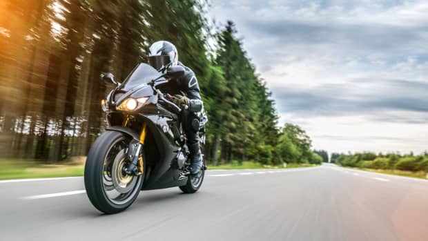 Motorradfahrer in schwarzer Lederkleidung fährt auf einer Landstraße am Waldrand