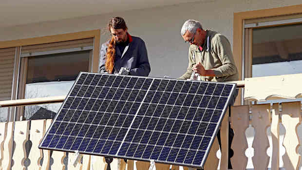 Zwei Männer installieren eine Solaranlage am Balkon