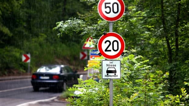 Ein Auto fährt bei Nässe um eine Kurve vorbei an einem Tempolimit-Schild