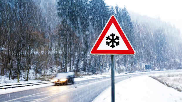 Ein im Winter fotografiertes Verkehrsschild mit einem Warndreieck und Schneeflocke darin befindend