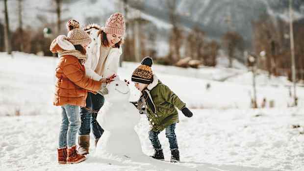 Eine Mutter baut mit ihren zwei Kindern einen Schneemann