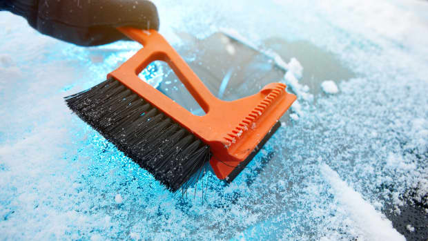 Hand räumt verschneite Autoscheibe mit einem Eiskratzer frei