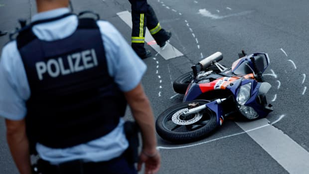 Ein Polizist steht vor einem verunfallten Motorrad auf einer Strasse
