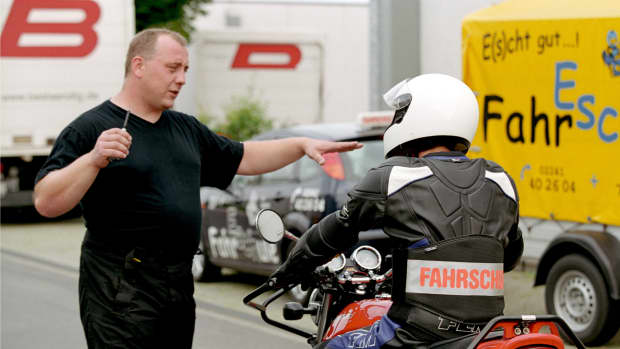 Ein Fahrschullehrer erklärt einem Schüler auf dem Motorrad die Regeln