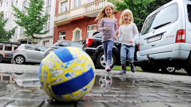 Zwei Mädchen laufen beim Spiel mit einem Ball über eine Straße