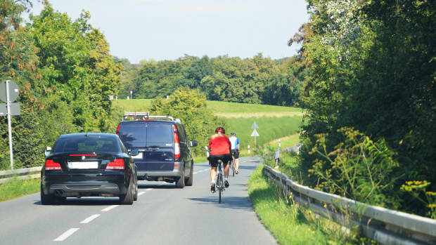 Zwei Autofahrer überholen zwei Radfahrer auf einer Landstraße