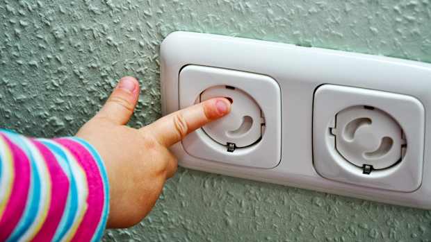 Ein Kleinkind mit Finger an Steckdose mit Kinderschutz zur Sicherheit des Kindes