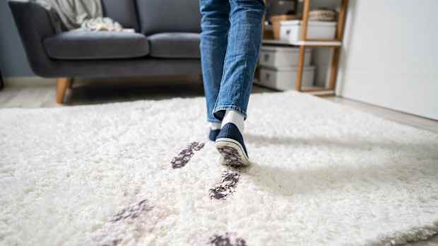 Ein junger Mann läuft mit schmutzigen Schuhen auf dem Teppich und hinterläßt Schmutzspuren